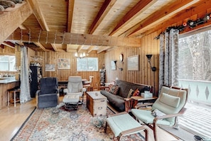 Interior de una cabaña de madera con sofá, sillas, una mesa de centro y una estantería.