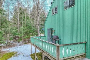 Una baita di legno verde con veranda, circondata da alberi.