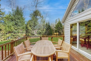 Eine Terrasse im Freien mit Holztisch und -stühlen, umgeben von einem Holzbalkon und einer Glastür zu einem Garten.