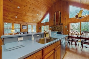 Ein Holzblockhaus-Interieur mit Küchenzeile, Holzschränken, einem Essbereich mit Stühlen und einem Steinkamin.