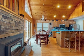 Ein Holzinterieur mit Kamin aus Stein, einem Essbereich und einer Küche mit Holzausstattung und einer blauen Arbeitsplatte.