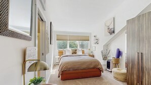 Ein Schlafzimmer mit Bett, Nachttischen, einem Kleiderschrank, einem Fenster und einem Spiegel.