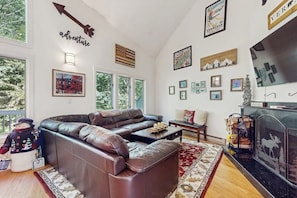 A living room with a sectional sofa, a fireplace, and various framed pictures on the walls. - Ski-in/ski-out townhouse w/ trail access, fireplace, balcony, pool, hot tub (Stratton)