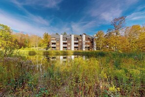 Ein mehrstöckiges Gebäude mit Balkonen, umgeben von einem Teich und Bäumen.