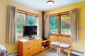 Ein Zimmer mit Fernseher auf einer Holzkommode, zwei Holzstühlen und einem Fenster mit Vorhängen.