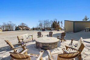 Ein mit Schnee bedeckter Außenbereich mit Adirondack-Stühlen und einer Steinkaminfeuerstelle.