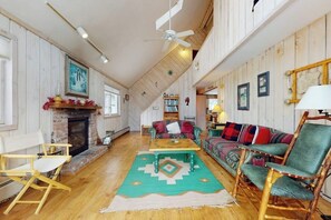 Ein geräumiges Wohnzimmer mit Kamin, Deckenventilator, Bücherregal und einem farbenfrohen Sofa.