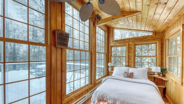 Ein Schlafzimmer in einer Blockhütte mit einem großen Bett, mehreren Fenstern und einem Deckenventilator.