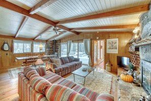 Ein gemütliches Blockhausschlafzimmer mit Holzbalkendecke, Kamin aus Naturstein, einer großen Couch und einem Essbereich.