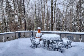 Ein mit Schnee bedeckter Außenbereich mit Essbereich, Metallstühlen und einem Tisch, umgeben von einem schneebedeckten Zaun und Bäumen.