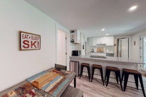 A modern kitchen with white cabinets, a central island with stools, and a sign on the wall.