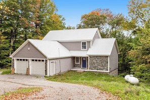 A two-story house with a garage, a stone exterior on the right side, and a gravel driveway.