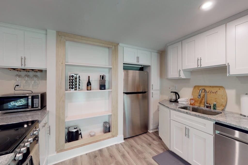 A modern kitchen with white cabinets, a stainless steel refrigerator, a microwave, and a built-in oven.