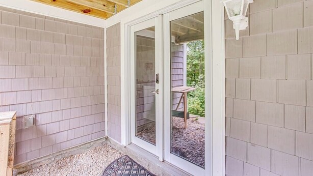 Un porche cubierto con techo de madera, puerta corredera de vidrio y pared exterior blanca.