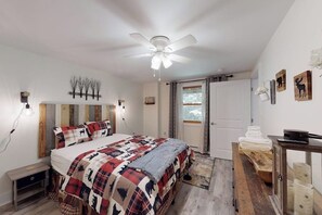 A bedroom with a bed, a ceiling fan, a nightstand, a dresser, and a door with a view.