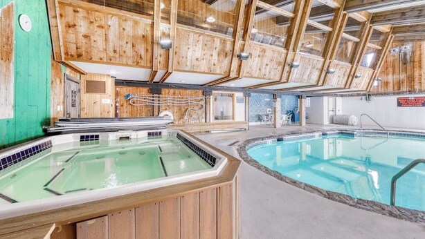 Ein Wellnessbereich mit Holzwandverkleidung, einer Whirlwanne und einem Schwimmbecken.