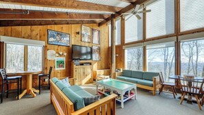 Ein gemütliches Blockhaus-Interieur mit Holzwänden, einem großen Fernseher und Blick ins Freie.