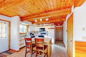 A kitchen with wooden ceiling beams, white cabinets, a central island with chairs, and a microwave. - Forest Home with Shared Pool & Hot Tub, WiFi, & Washer/Dryer - One Small Dog OK (Wilmington)