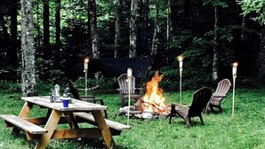 En picknickplats med en eldplats, stolar och ett bord i en skog.
