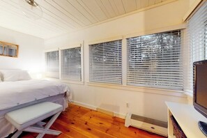 Une chambre à coucher avec un lit, un banc et trois fenêtres équipées de stores.
