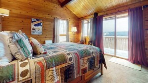 A wooden cabin room with a large bed, a window with curtains, and a view of the outside. - Inviting mountain view home with game room, balcony & W/D (West Dover)