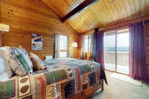 Ein Zimmer in einer Holzhütte mit einem großen Bett, einem Fenster mit Vorhängen und Blick nach draußen.