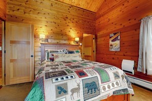 Ein Schlafzimmer einer Holzhütte mit einer gesteppten Bettdecke, einem aufgehängten Poster und einem Heizgerät.