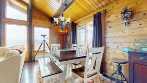 A wooden cabin interior with a dining table, white chairs, a chandelier, and a tripod in the corner. - Inviting mountain view home with game room, balcony & W/D (West Dover)