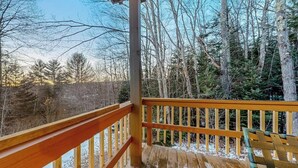 Une terrasse en bois avec une rambarde, entourée d’arbres et sous un ciel dégagé.