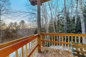 A wooden deck with a railing, surrounded by trees and a clear sky.