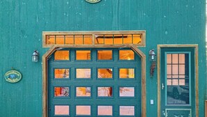 Un bâtiment vert doté d’une grande porte de garage et d’une petite porte avec une fenêtre.