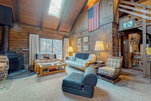 A log cabin interior with a sofa, armchair, and a fireplace.