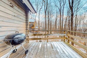 A wooden deck with a barbecue grill, a wooden fence, and a view of a forested area.