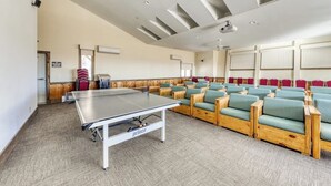 A conference room with a ping pong table, rows of chairs, a ceiling fan, and a projector. - Classic Vermont cabin with forest views, pools, hot tub & gym (Wilmington)