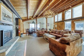 A spacious living room with a fireplace, wooden ceiling beams, and large windows.