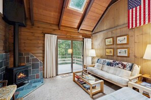 L’intérieur d’un chalet accueillant, avec une cheminée, un canapé, une table basse et une vue à travers une porte vitrée.