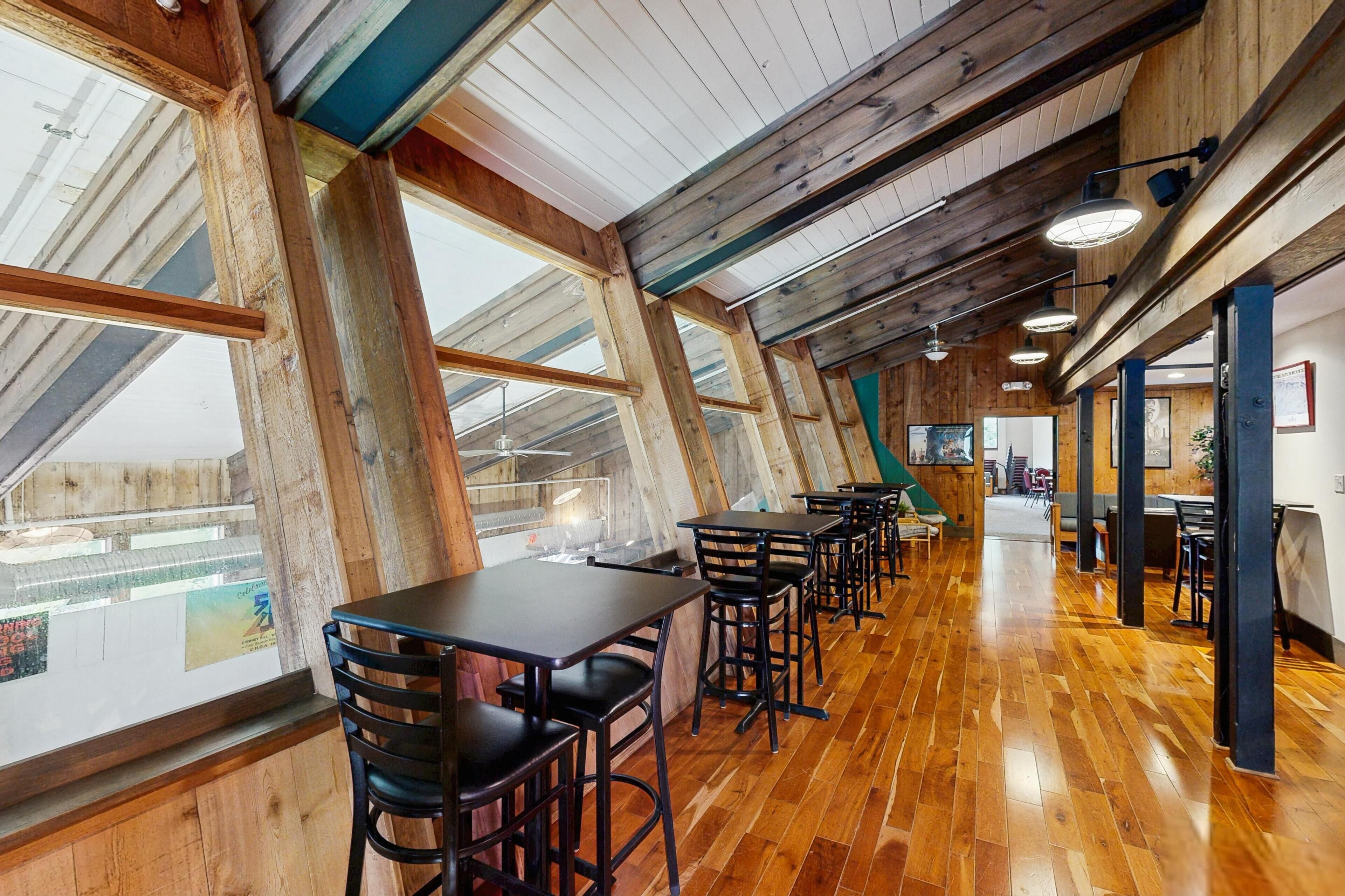 A spacious indoor area with high ceilings and wooden beams, featuring multiple tables and chairs arranged for dining or socializing.