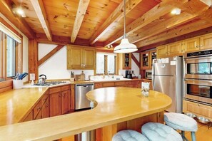 Una cocina con armarios de madera, un refrigerador de acero inoxidable, horno empotrado y una isla grande con taburetes.