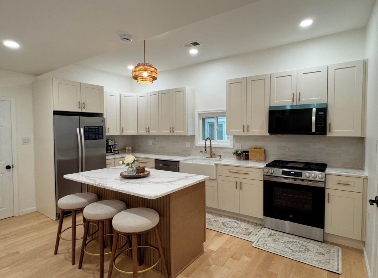 A modern kitchen with a central island, bar stools, stainless steel appliances, and light-colored cabinetry.