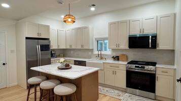 A modern kitchen with a central island, bar stools, stainless steel appliances, and light-colored cabinetry.