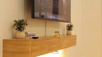 A flat-screen TV mounted on a wooden console with two potted plants, a remote control, and a few books.