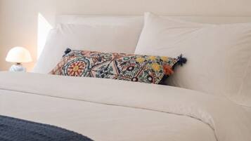 A bedroom with a bed, a colorful pillow, a lamp, and a painting of a beach scene.