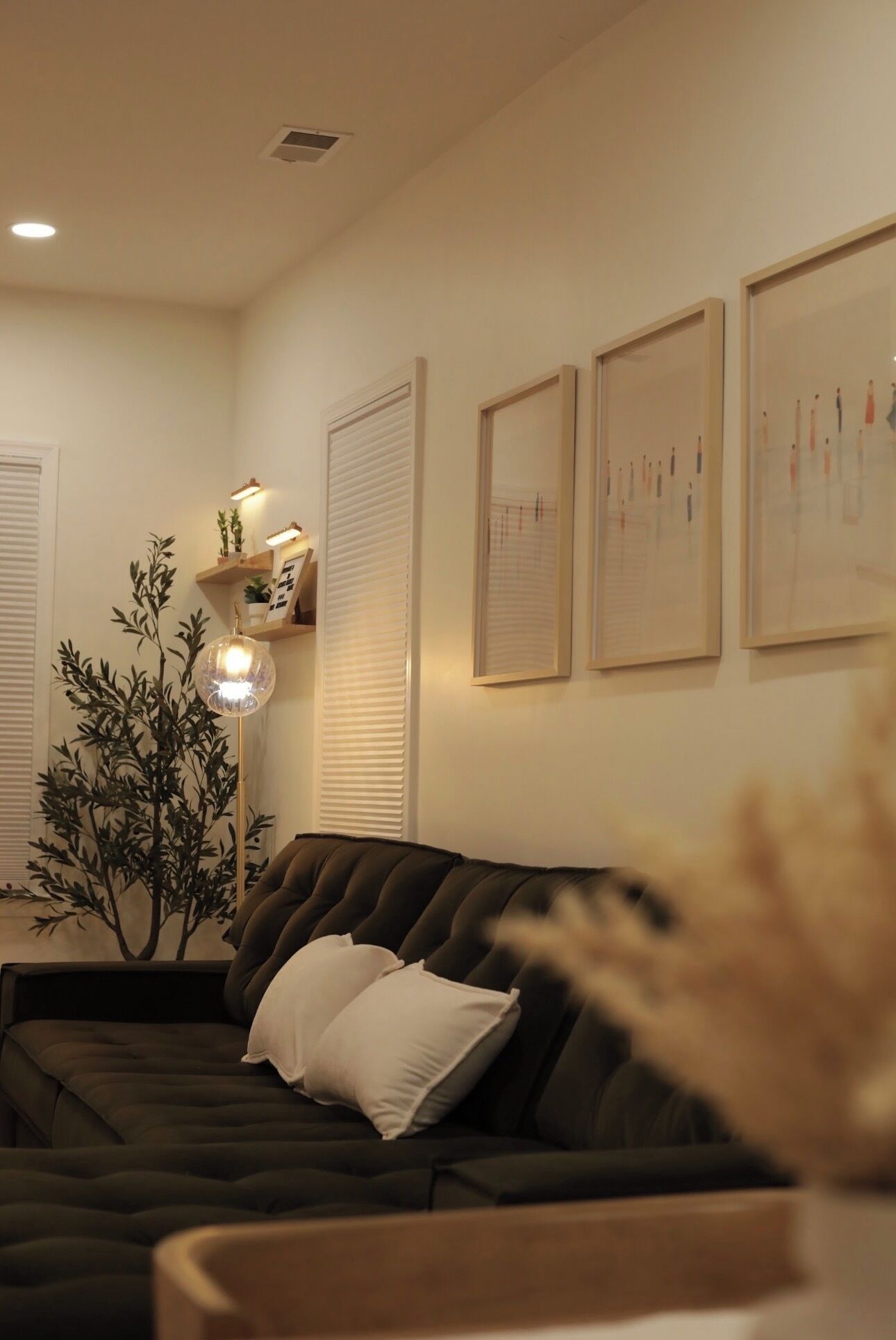 A living room with a dark sofa, a floor lamp, and wall-mounted blinds.