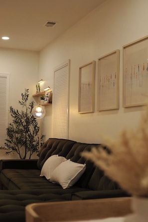 Ein Wohnzimmer mit einer dunklen Couch, einer Stehlampe und Wandjalousien.