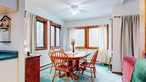 A dining area with a wooden table and chairs, a ceiling fan, and windows with curtains.