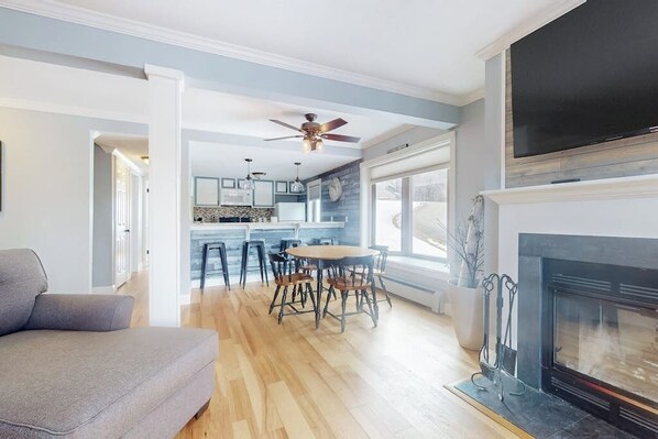 Una sala de estar moderna con chimenea, comedor y cocina al fondo.