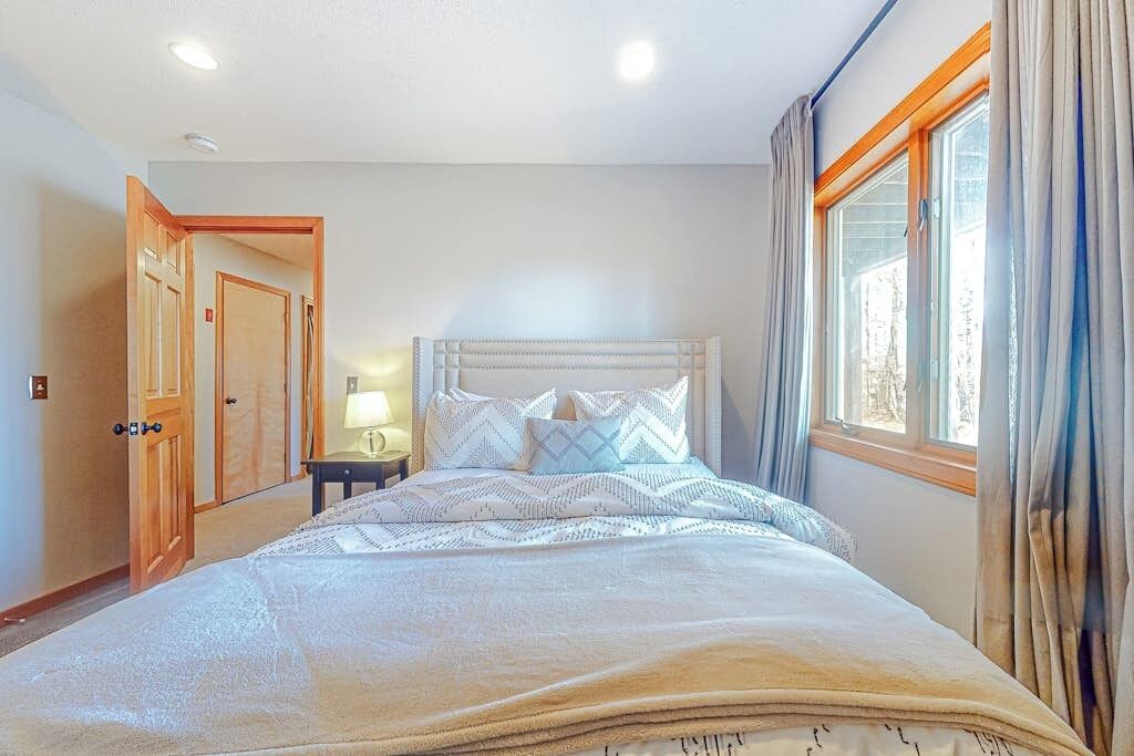 A bedroom with a bed, a nightstand, a lamp, and a window with curtains.