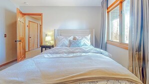 Ein Schlafzimmer mit Bett, Nachttisch, Lampe und einem Fenster mit Vorhängen.
