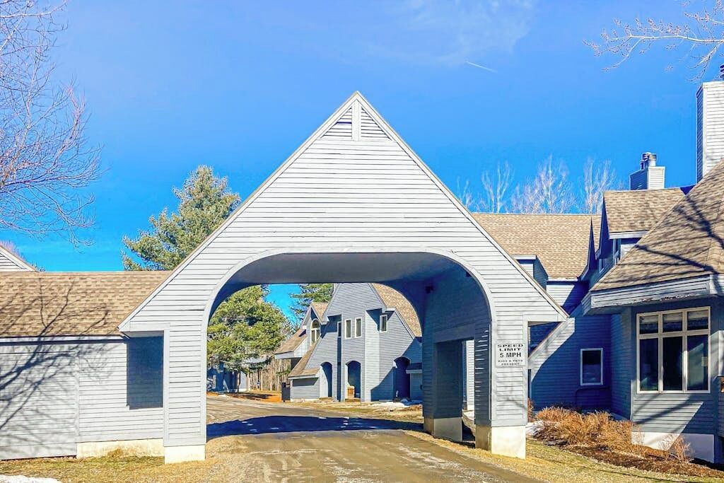 Une rue résidentielle bordée de maisons, avec un panneau indiquant la limite de vitesse et une structure en forme d’arc.