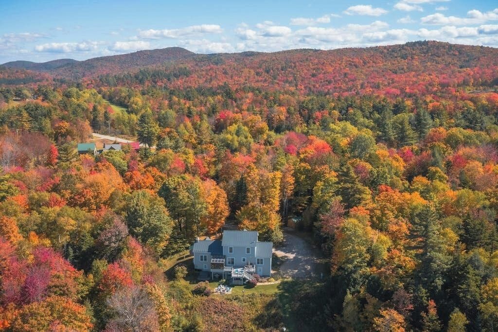 A large house surrounded by a forest with autumn foliage.